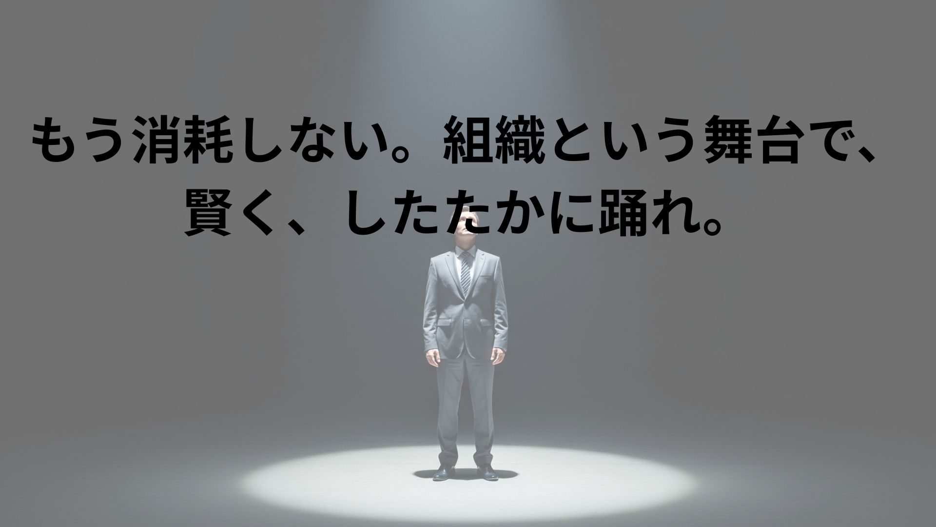 広大で暗い舞台の中央に、上からのスポットライトに照らされて一人の人物が立っている。顔ははっきりと見えないが、光を見上げているように見え、ドラマチックで思慮深いシルエットを作り出している。組織という大きな構造の中での、戦略的思考と個性を象徴する画像。
