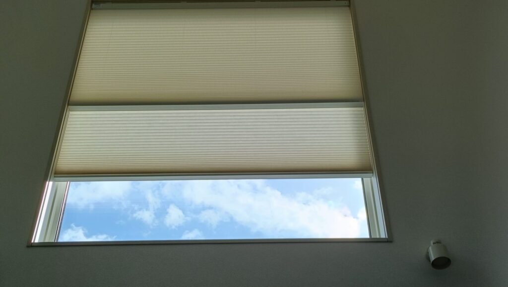 南面の大開口窓に設置した電動ハニカムシェードを半分開けた状態。上部で日差しを遮りつつ、下部から青空を取り込み、光と開放感を両立している。