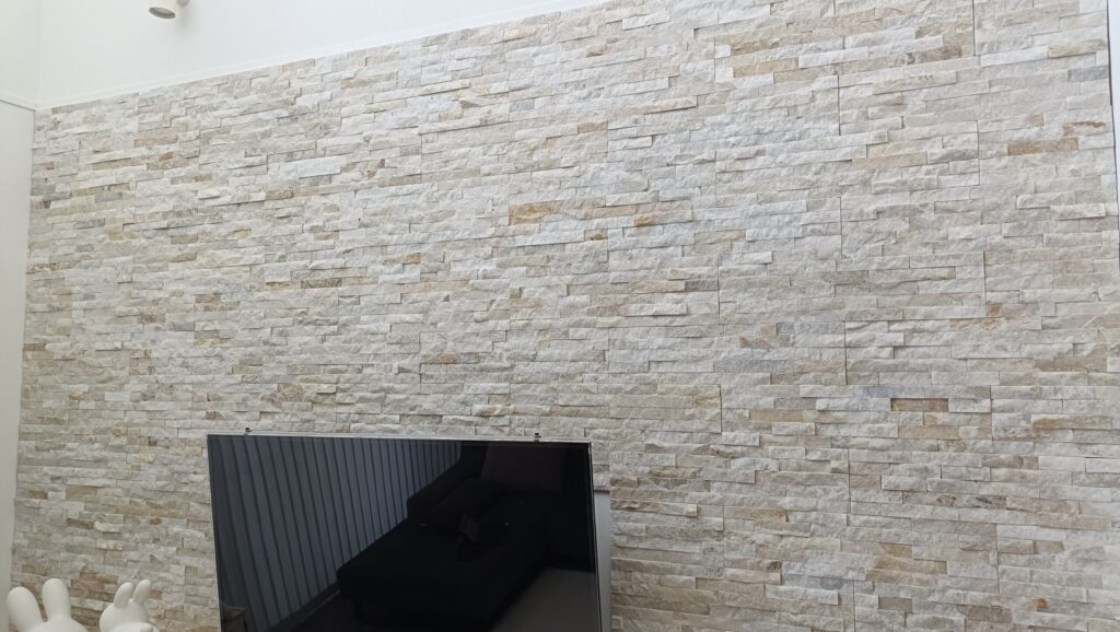 一条工務店グランスマートのリビング正面に施工したバンピーウォール。天然石の凹凸が美しく、55型の壁掛けテレビと調和した上質な空間を演出している。