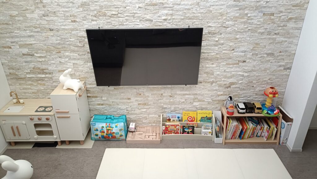 一条工務店グランスマートのリビングに設けた子どもスペース。バンピーウォールを背景に、壁掛けテレビの下におままごとキッチンや本棚を配置し、家族が動きやすく過ごせるよう工夫されている。